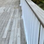 Wooden deck with white railing and greenery.