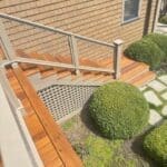 Wooden deck and stairs with green shrubs.