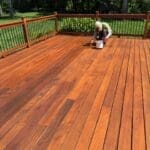 Person staining large wooden deck outdoors.