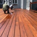 Workers staining a wooden deck outside house.