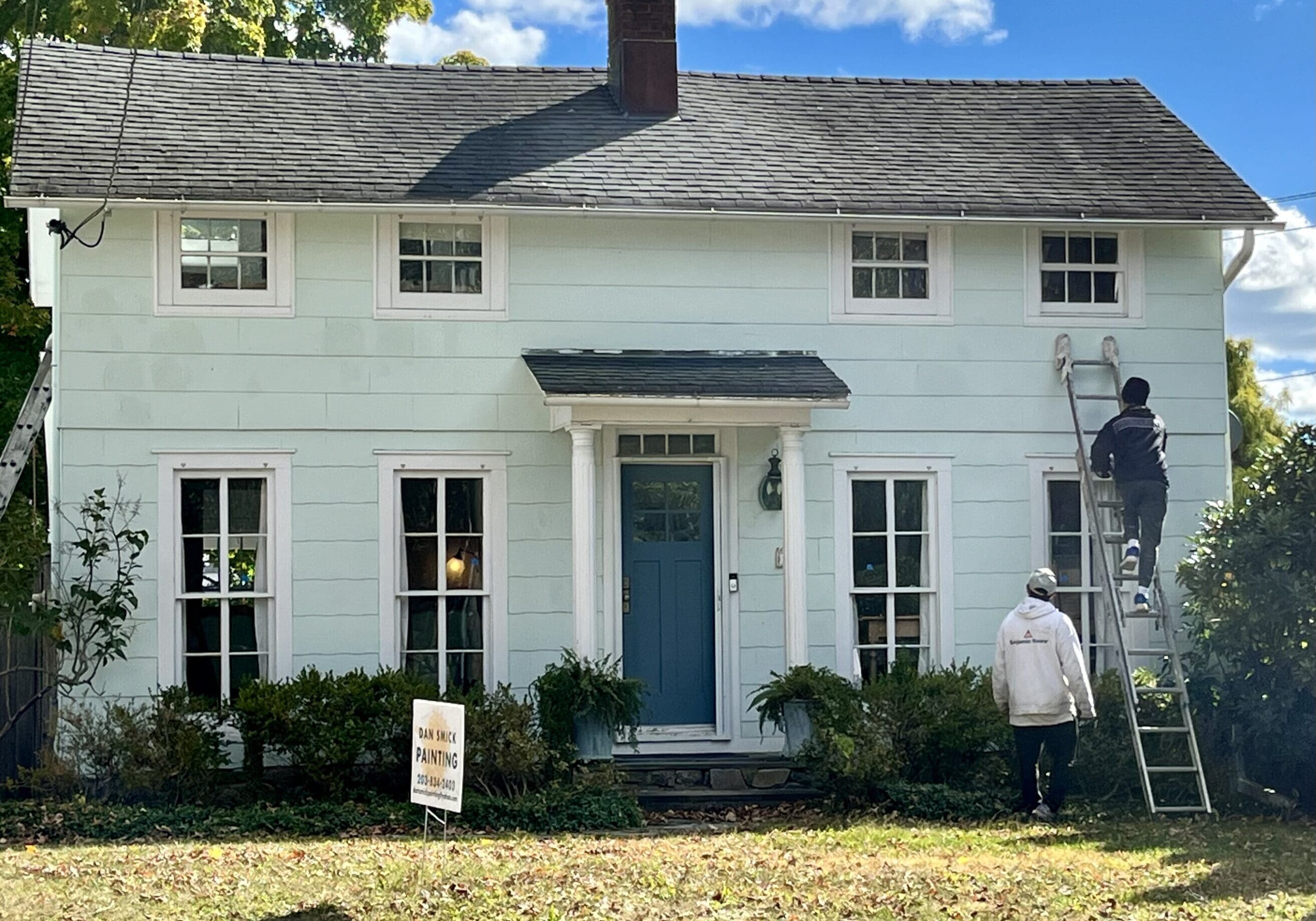 A man standing on the ladder outside of a house.